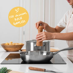 Unbeschichtete Edelstahlpfanne auf dem Induktionsfeld, darüber wird mit der Pfeffermühle gewürzt.